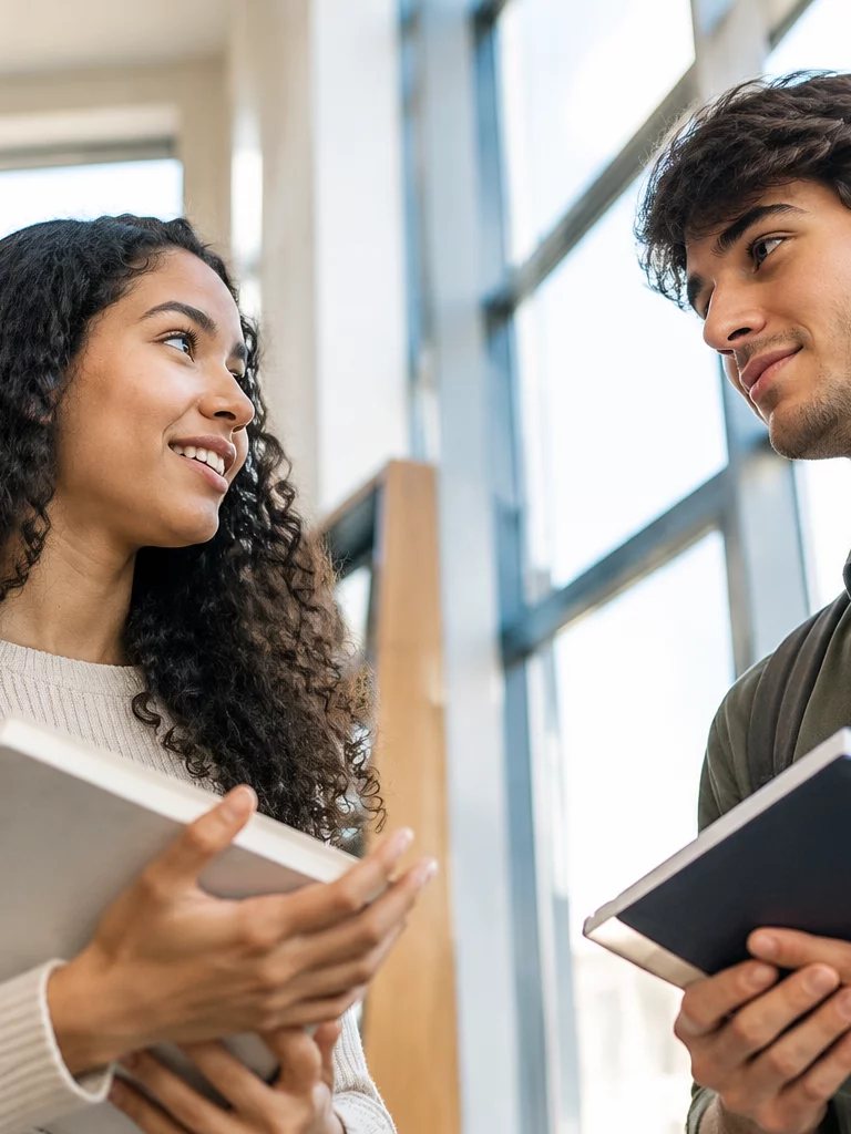 Duas participantes conversando de pé no corredor entre prateleiras de livros
